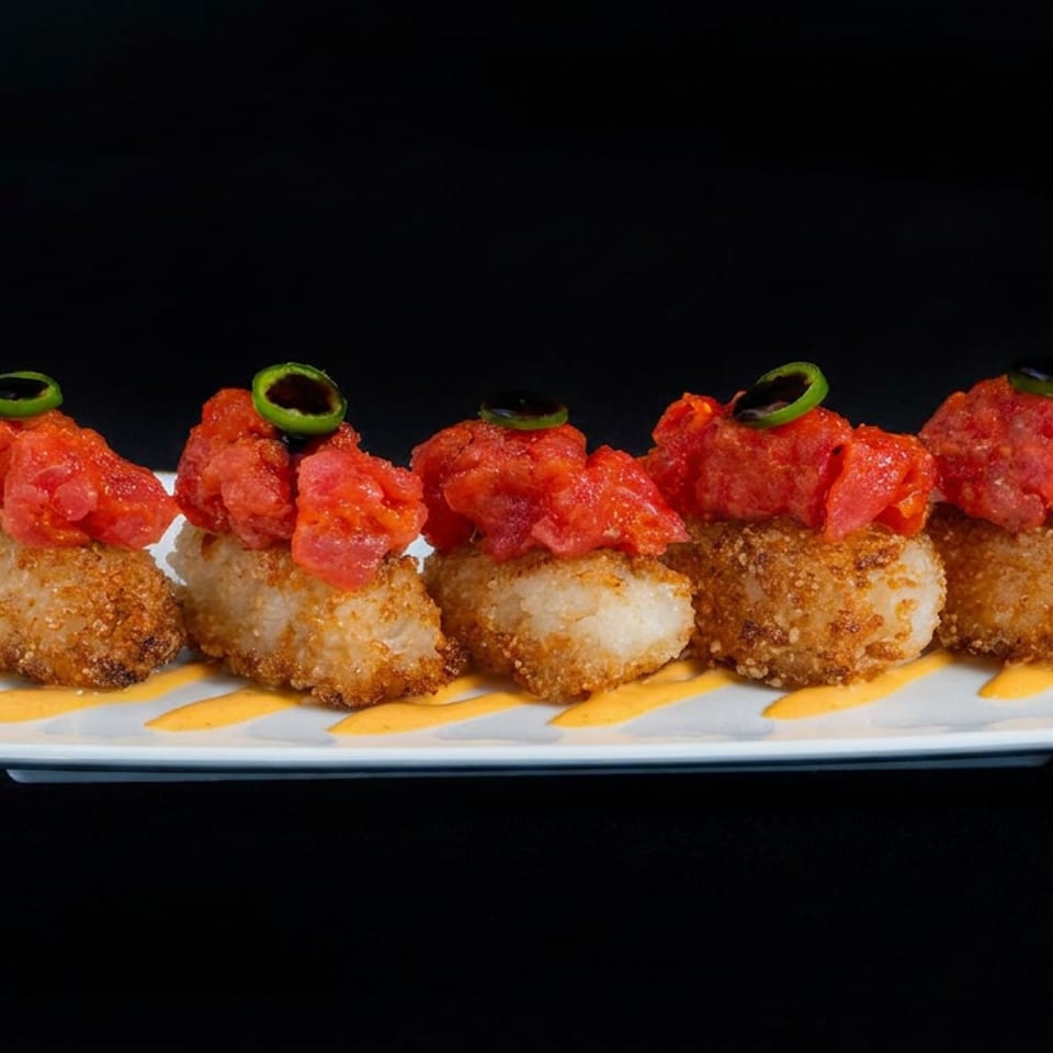 Crispy golden bites topped with diced red peppers and jalapeño rings, arranged on a white plate with orange sauce.