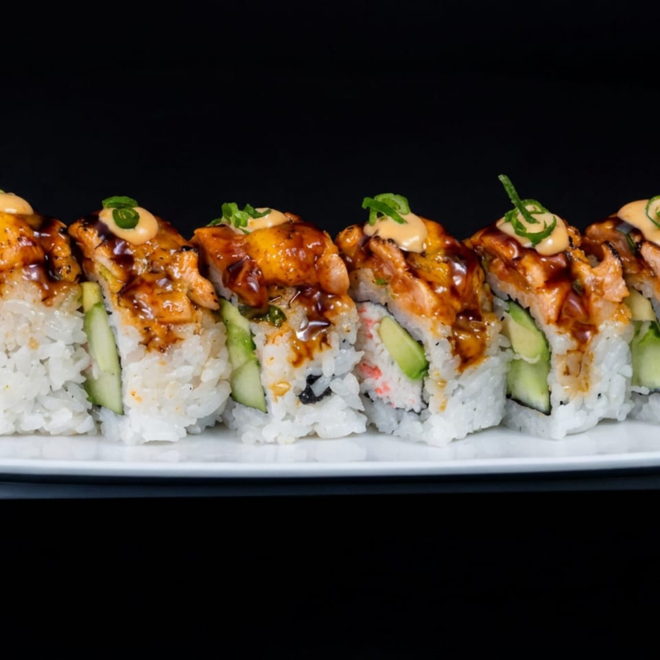 Sushi roll pieces topped with glazed chicken, spicy mayonnaise, and sliced green onions on a white rectangular plate.