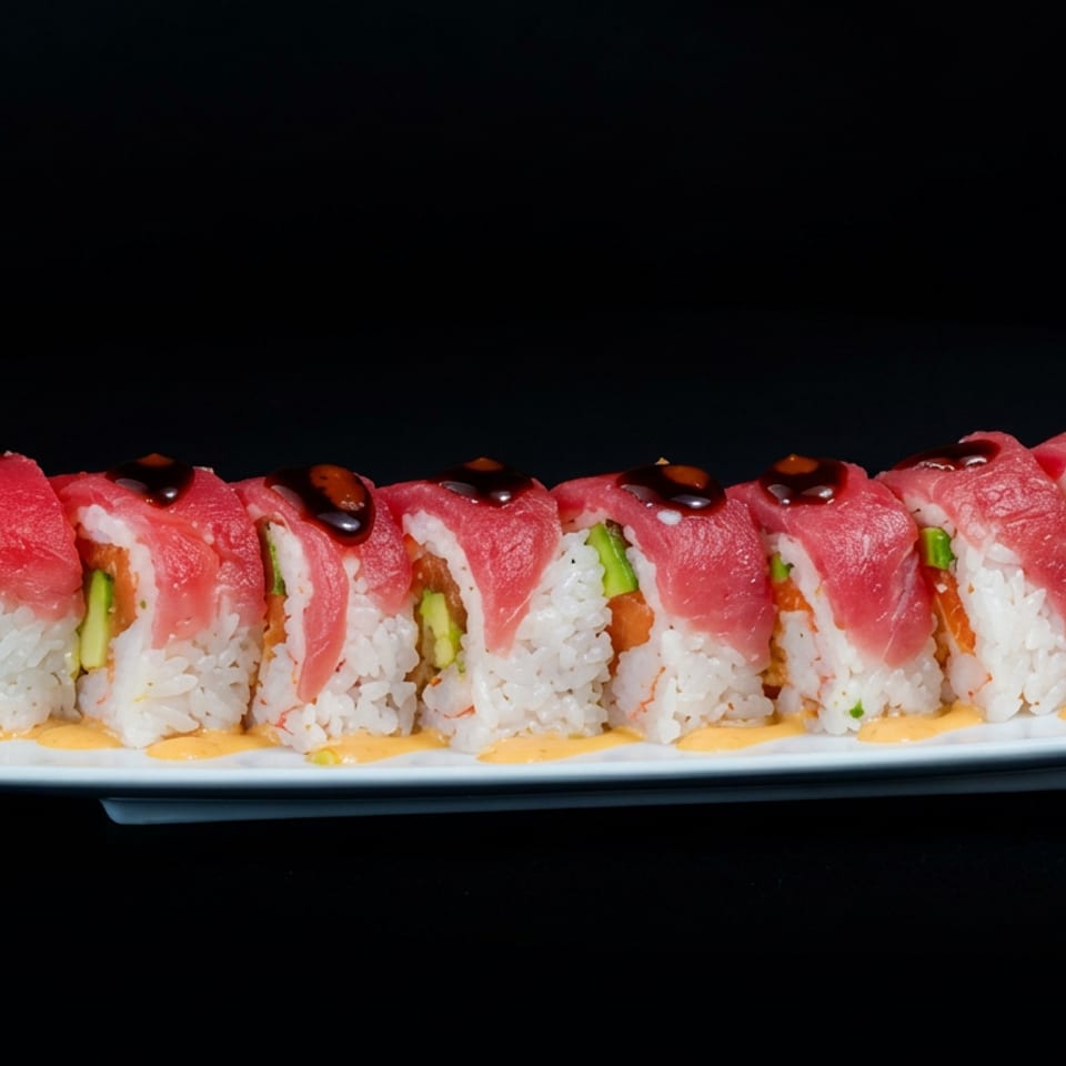 Sushi roll topped with fresh tuna, rice, shrimp tempura, vegetables, and dark sauce on a white rectangular plate.